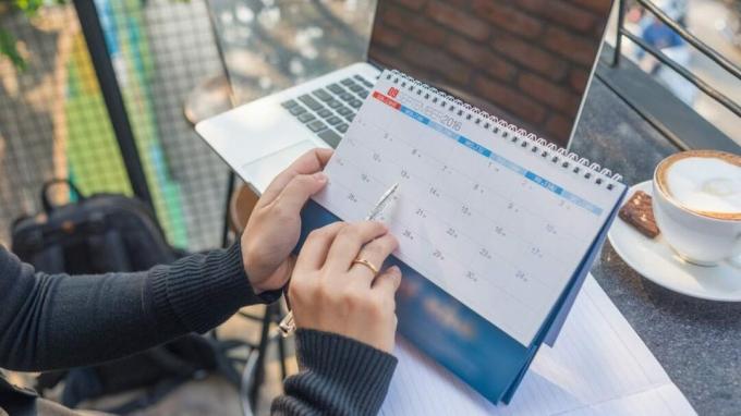 Mutter mit ADHS zeigt auf Kalender mit Stift und Laptop in der Nähe